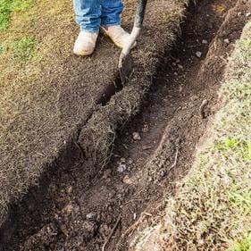 A person digging in the ground with a shovel.