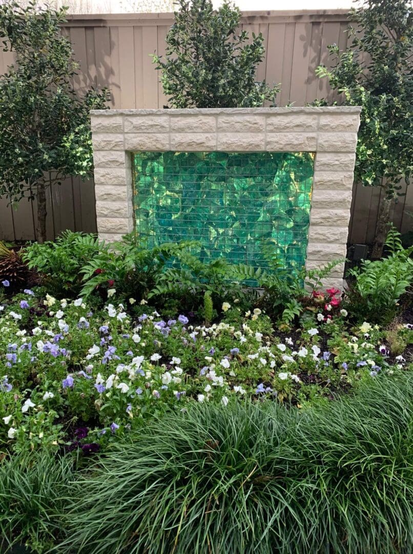 A green and white brick wall in the middle of some flowers.