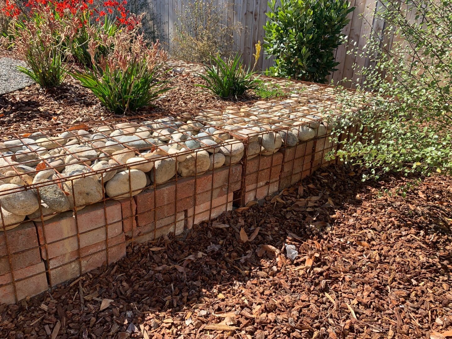 A brick wall with rocks and leaves on the ground.