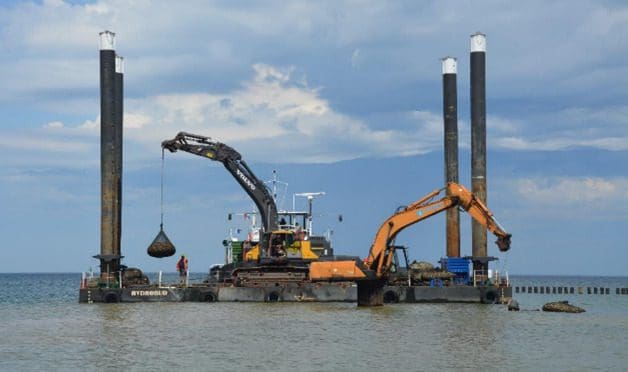 A large crane is in the water near two other cranes.