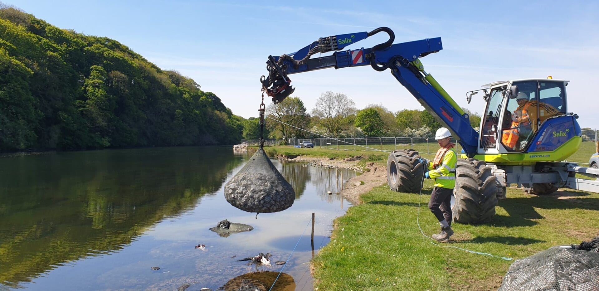 A crane is lifting a bag of debris into the water.